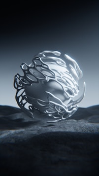 A futuristic, abstract metallic sculpture with flowing, organic shapes stands on a textured surface. The lighting casts intricate shadows, enhancing the three-dimensional appearance.