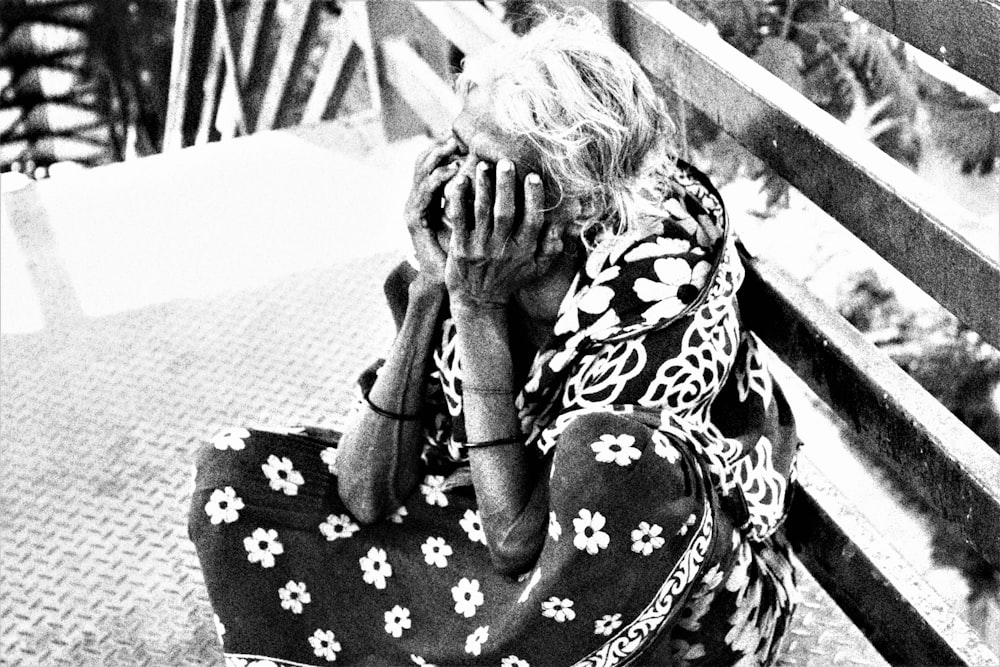 a woman sitting on a bench covering her face