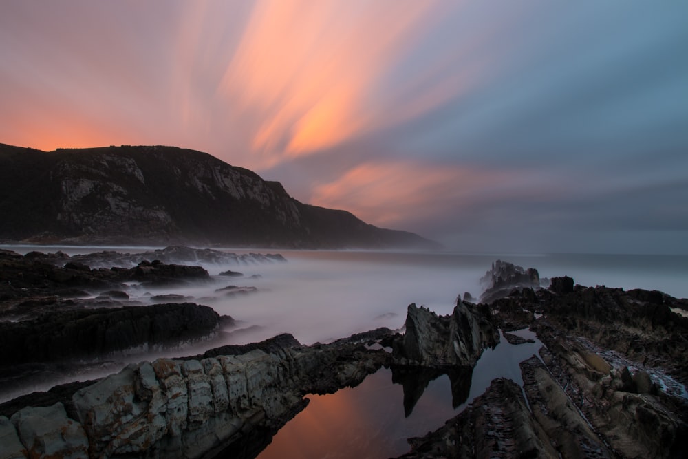 Una larga exposición de una puesta de sol sobre una playa rocosa