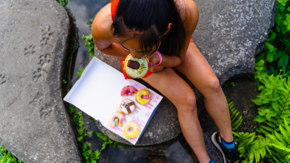 a woman sitting on a rock with a box of donuts