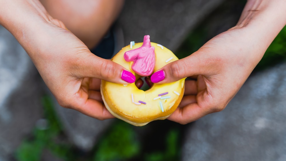 a person holding a yellow doughnut with pink frosting