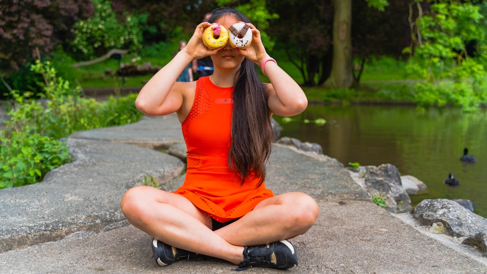 a woman in an orange dress sitting on a rock with a donut in her