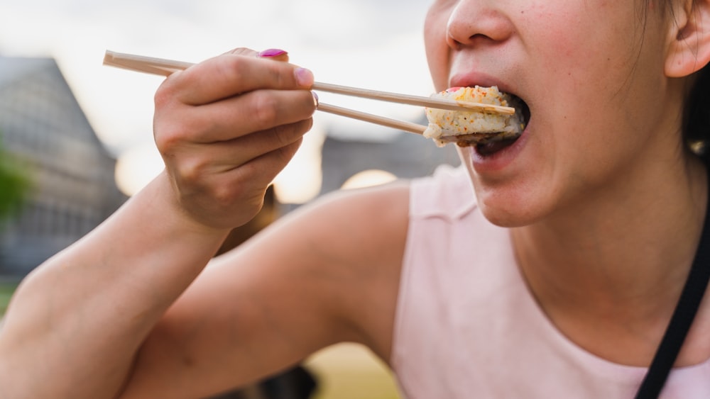 a woman eating a piece of food with chopsticks