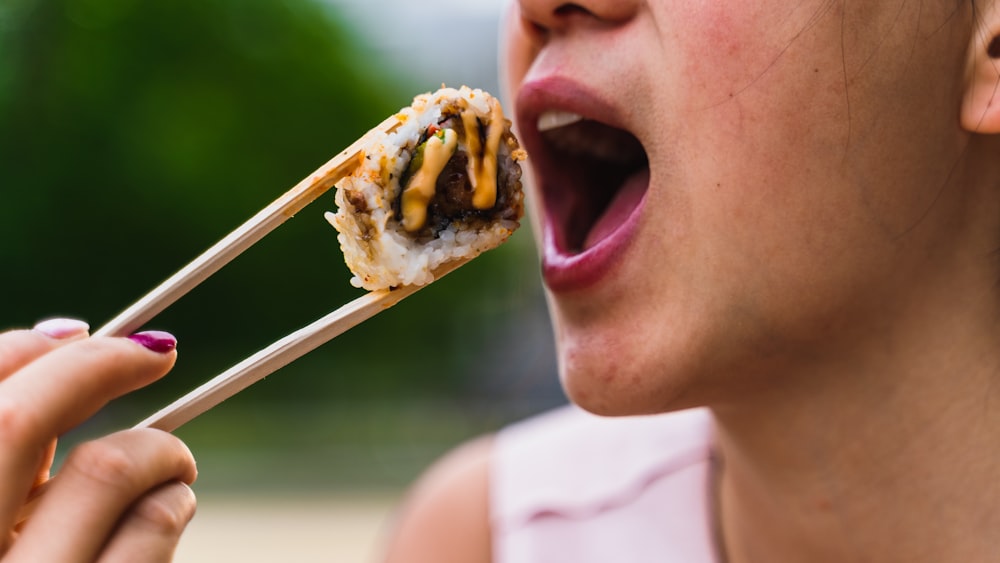 a woman eating a piece of food with chopsticks