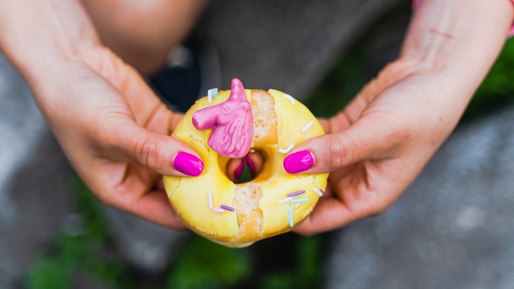 a person holding a donut with a pink frosting and sprinkles