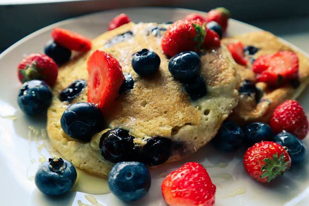 Un plato blanco cubierto con panqueques cubiertos de arándanos y fresas