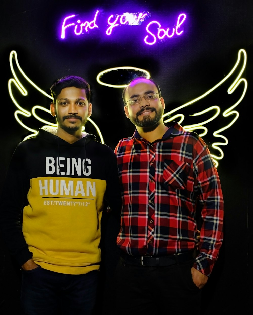 two men standing next to each other in front of a neon sign
