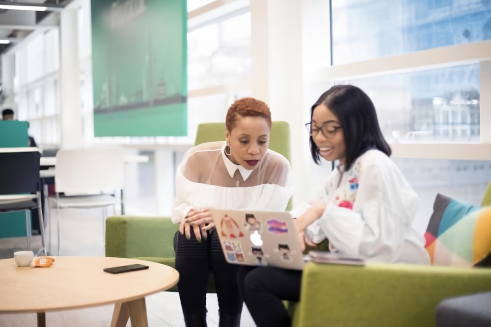 two women sitting on a couch looking at a laptop