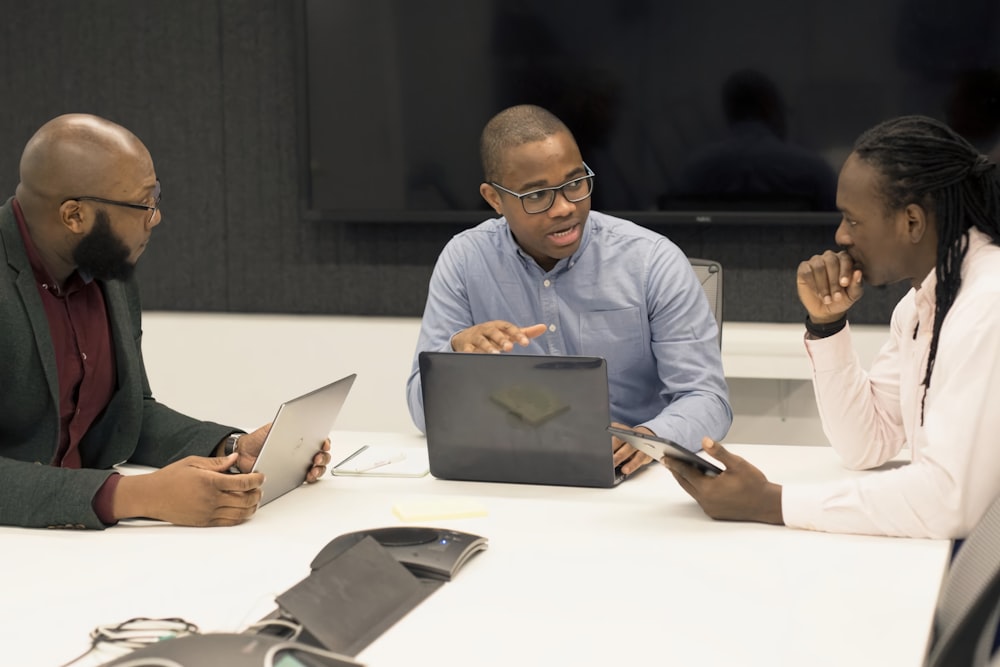 a group of people sitting around a table with laptops