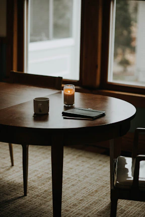 A cozy nook with a dark wooden table, a latte, and an open dot-grid journal surrounded by soft floral accents.