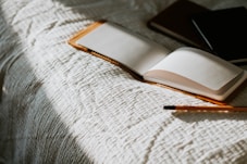an open book sitting on top of a bed next to a pencil