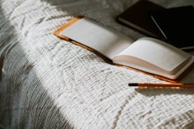 an open book sitting on top of a bed next to a pencil