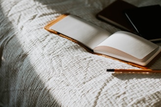 an open book sitting on top of a bed next to a pencil