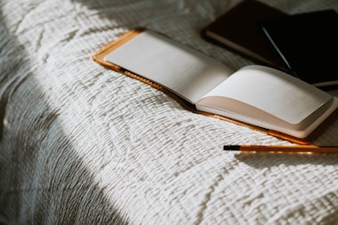 an open book sitting on top of a bed next to a pencil