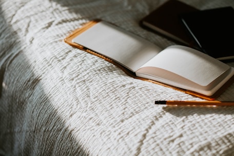 an open book sitting on top of a bed next to a pencil