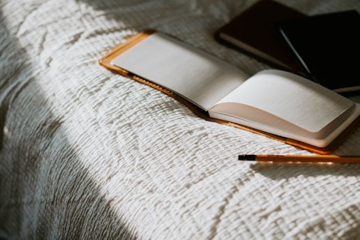an open book sitting on top of a bed next to a pencil