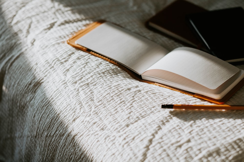 an open book sitting on top of a bed next to a pencil