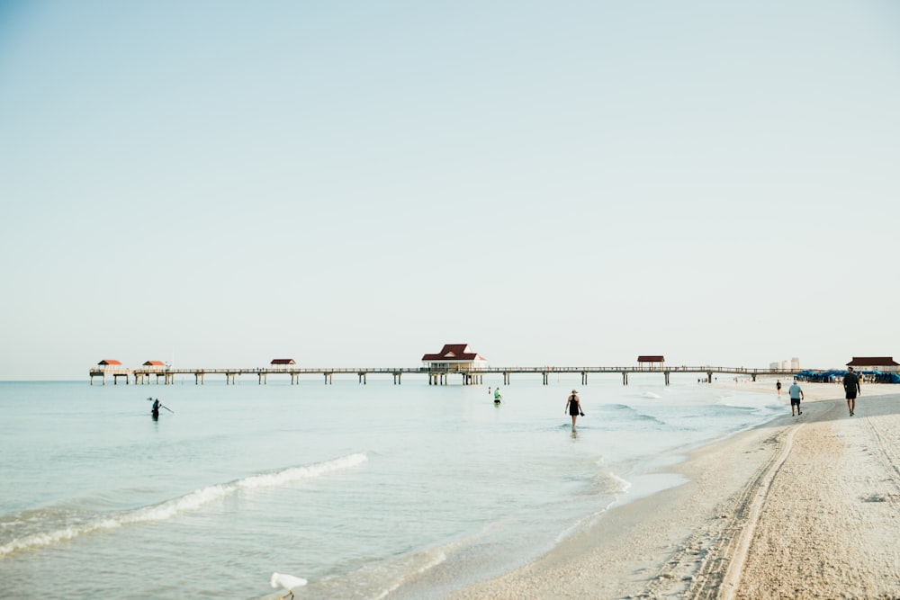 people are walking on the beach near a pier