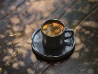 Freshly brewed hot coffee served in a rustic ceramic cup with morning sunlight filtering through leaves.