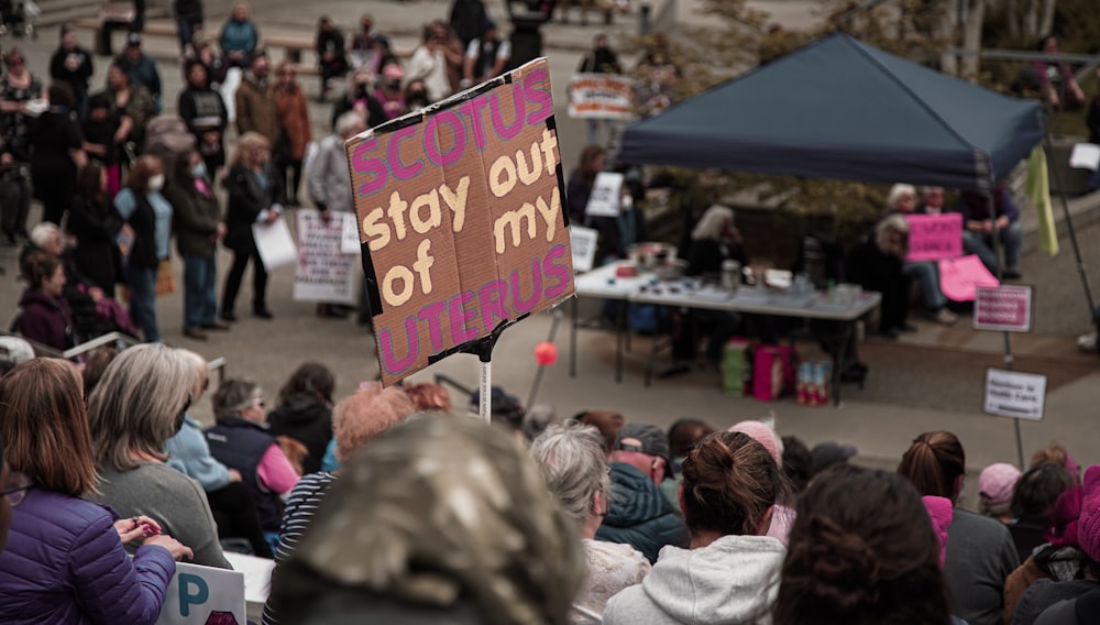 a crowd of people standing around a table with a sign