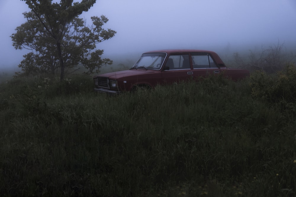 Une vieille voiture est assise dans un champ par une journée brumeuse