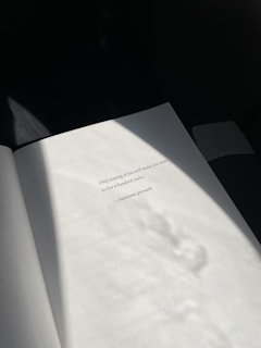 An open book page is illuminated by soft, natural light, revealing a printed quote attributed to a Japanese proverb. The shadows cast create a tranquil and contemplative atmosphere.
