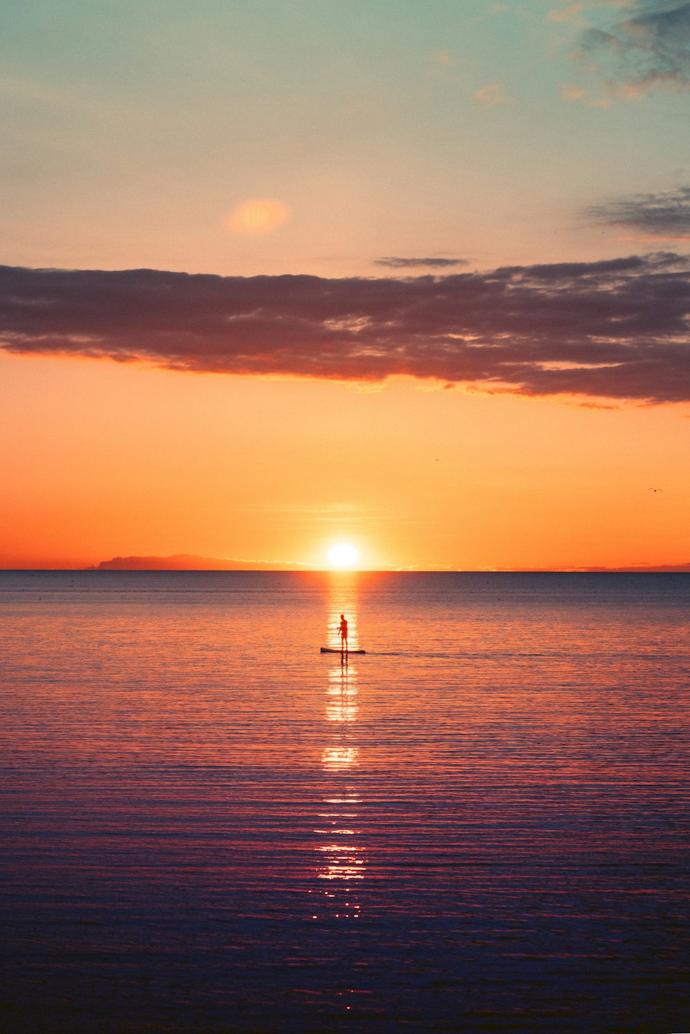 a person standing on a surfboard in the ocean at sunset