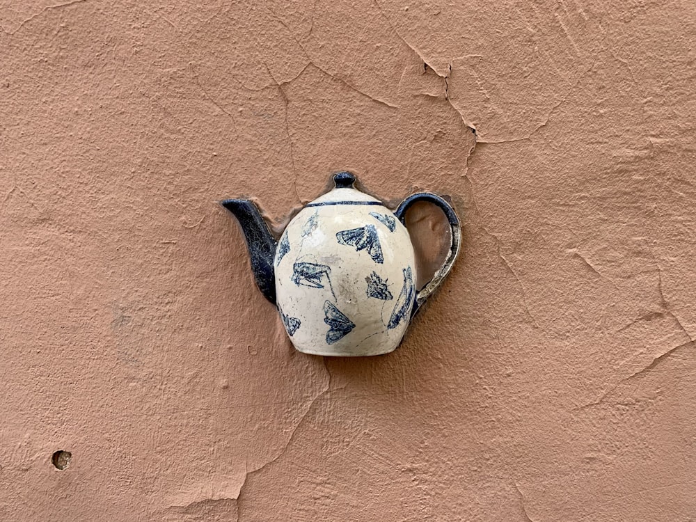 a teapot with a blue design on it hanging on a wall