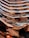 An intricate, modern architectural structure with multiple levels and glass railings, featuring a metallic copper finish that creates reflections and varying patterns. The design has a honeycomb-like appearance with angular, geometric shapes dominating the composition.