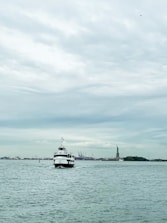 Tourists enjoying a guided boat tour with a guide pointing towards the Statue of Liberty under a clear blue sky.