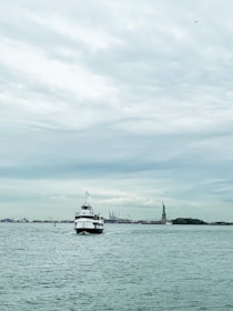 Tourists enjoying a guided boat tour with a guide pointing towards the Statue of Liberty under a clear blue sky.