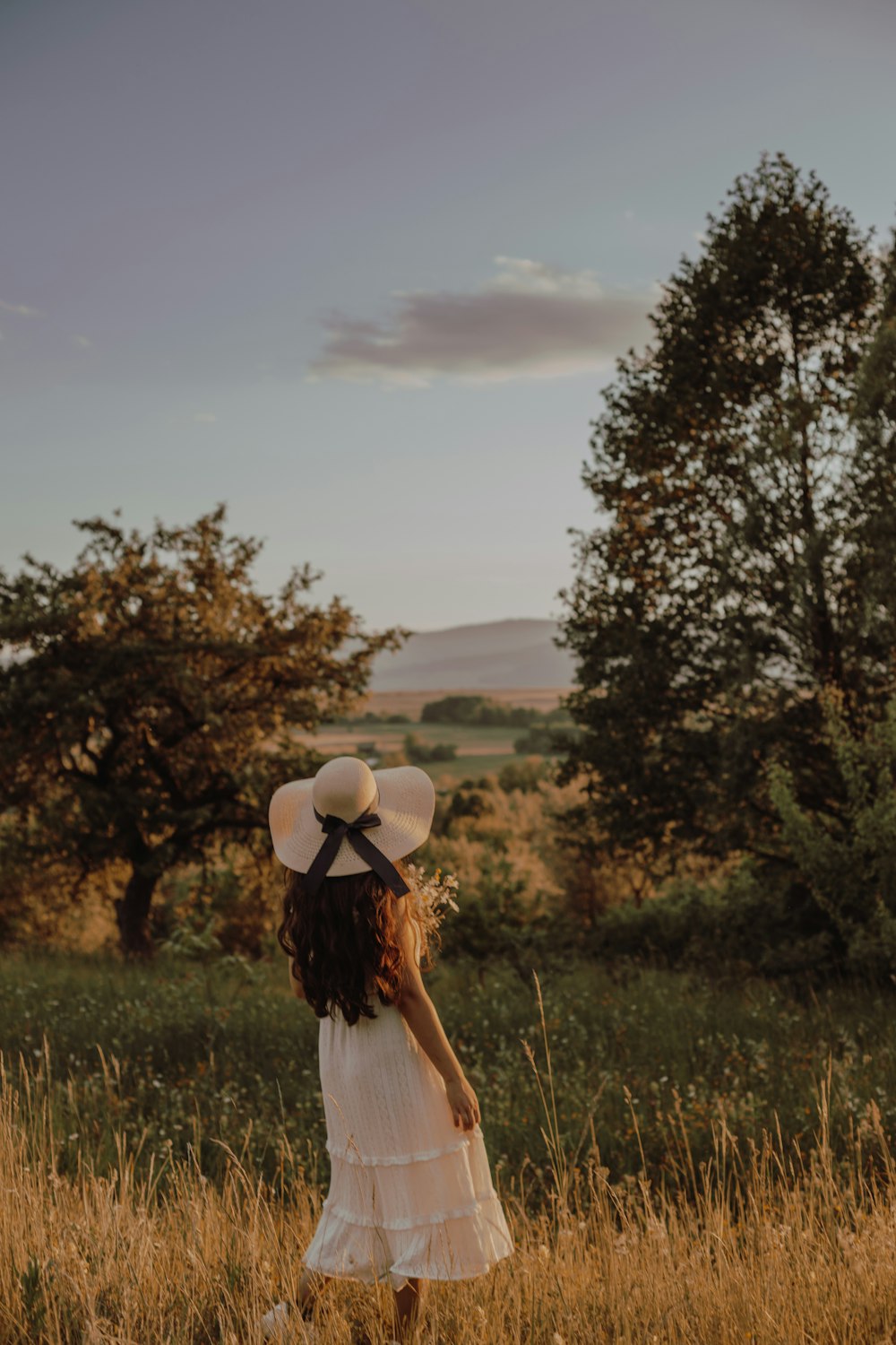 a little girl in a white dress and hat standing in a field
