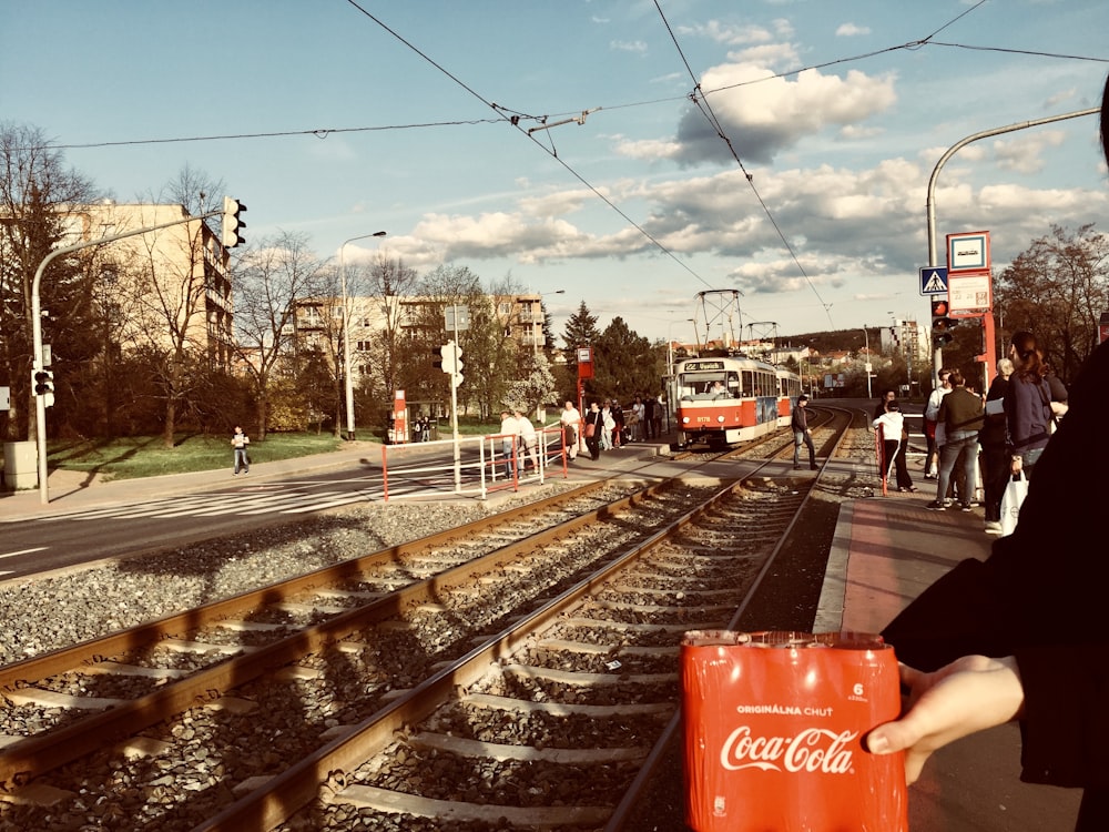 a woman holding a can of coca - cola on a train track