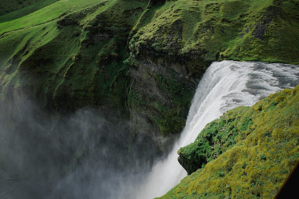 a large waterfall with a lush green hillside in the background