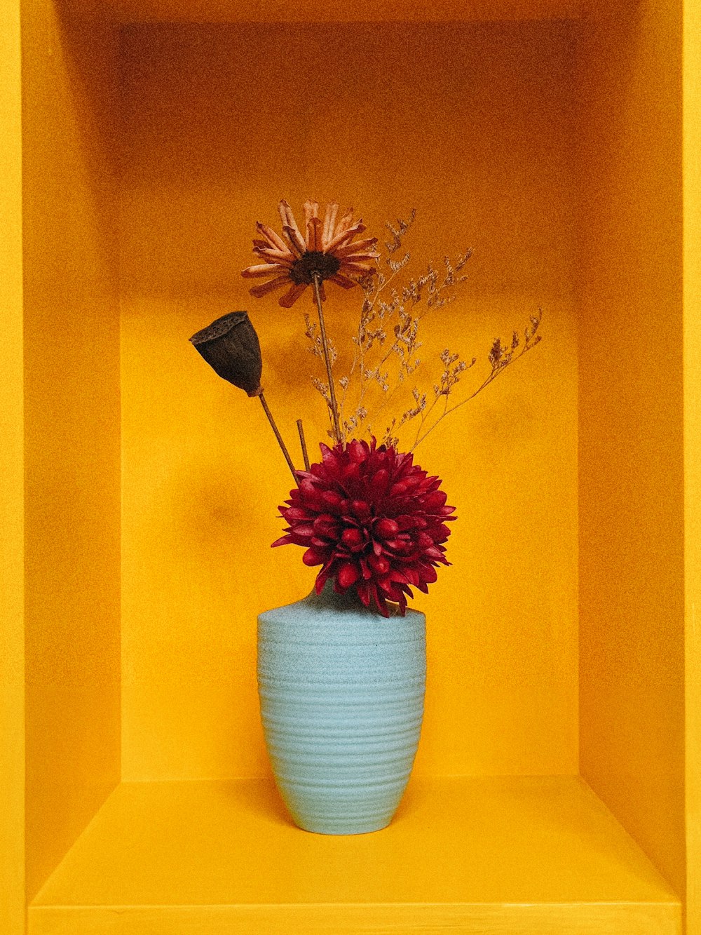 un vase bleu avec une fleur rouge dedans