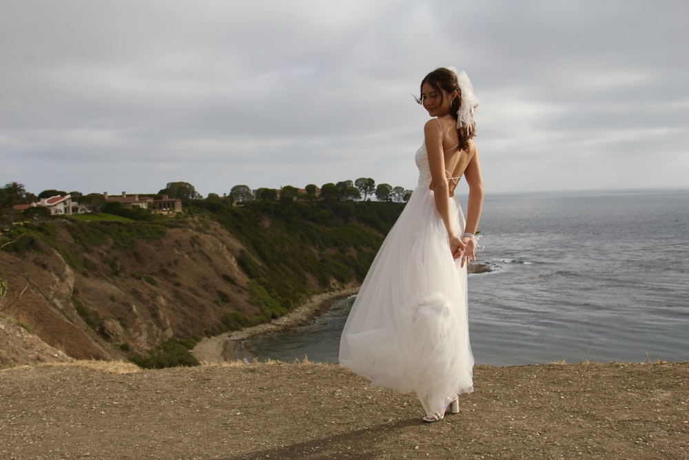 a woman in a wedding dress standing on a cliff overlooking the ocean