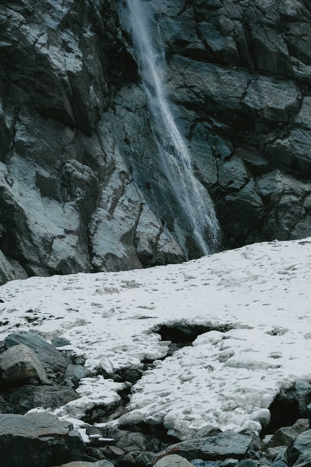 a man standing on top of a snow covered slope next to a waterfall