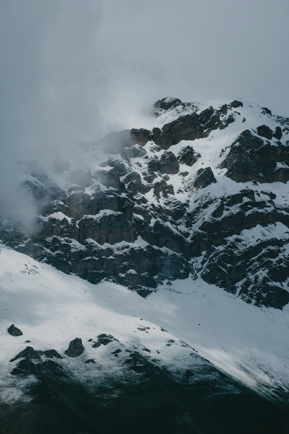 a mountain covered in snow and clouds on a cloudy day