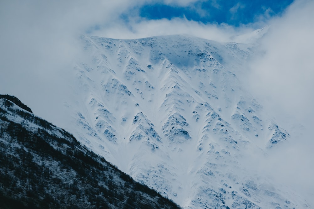 a mountain covered in snow and clouds under a blue sky