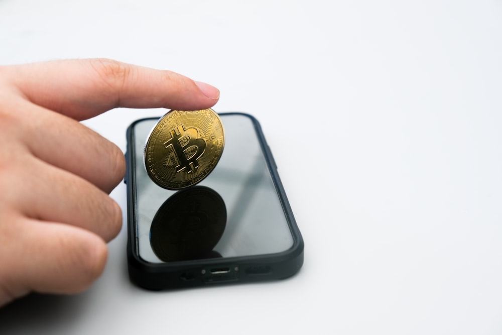 uma pessoa segurando uma moeda de ouro na frente de um telefone celular