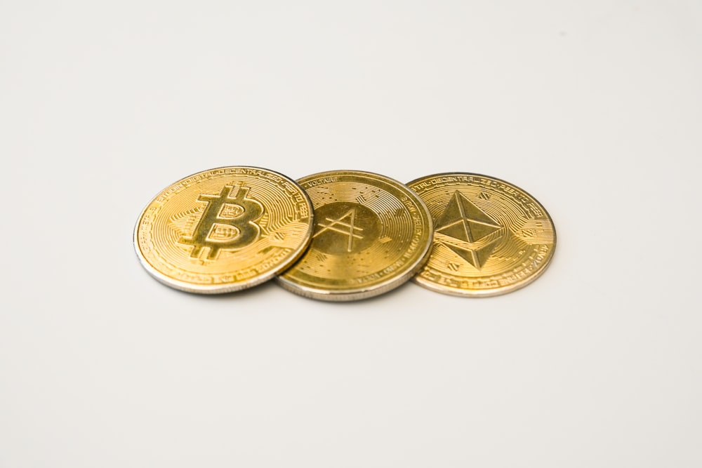 three gold bitcoins sitting side by side on a white surface