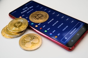a cell phone with a bitcoin on it next to a pile of coins
