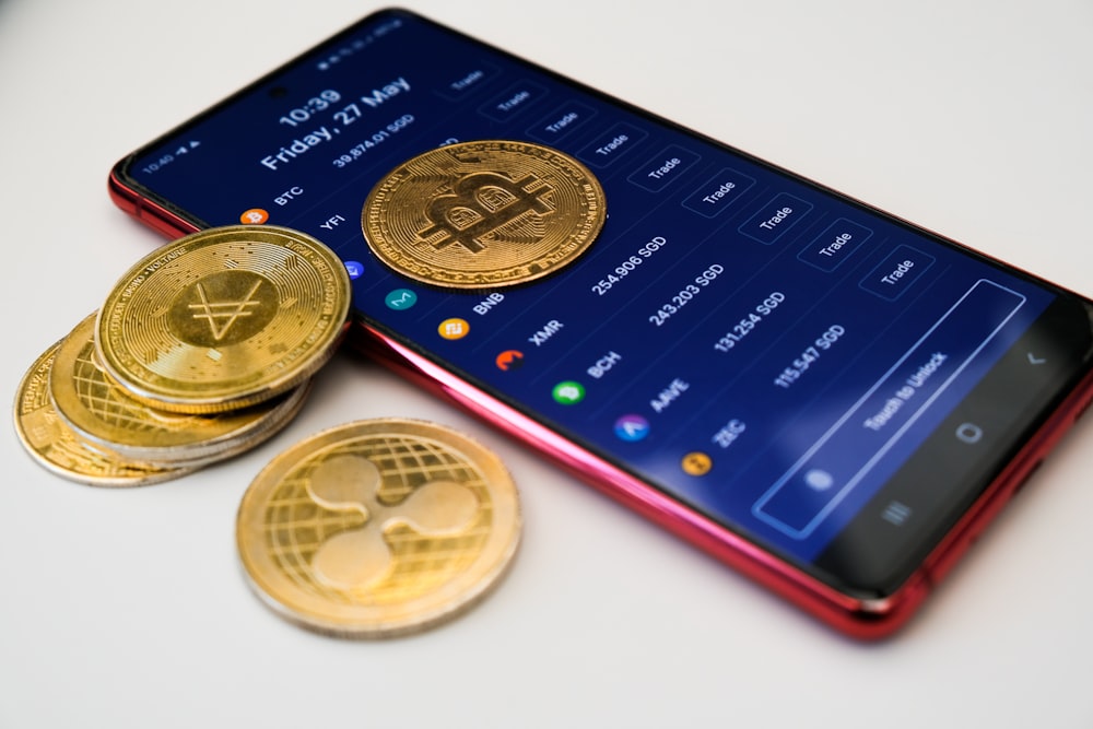 a cell phone with a bitcoin on it next to a pile of coins