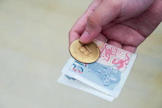 Close-up of hands holding gold coins and financial documents with charts in the background.