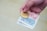 A hand is holding a gold Bitcoin coin and a few paper banknotes. The background is plain and out of focus.