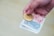 A hand is holding a gold Bitcoin coin and a few paper banknotes. The background is plain and out of focus.