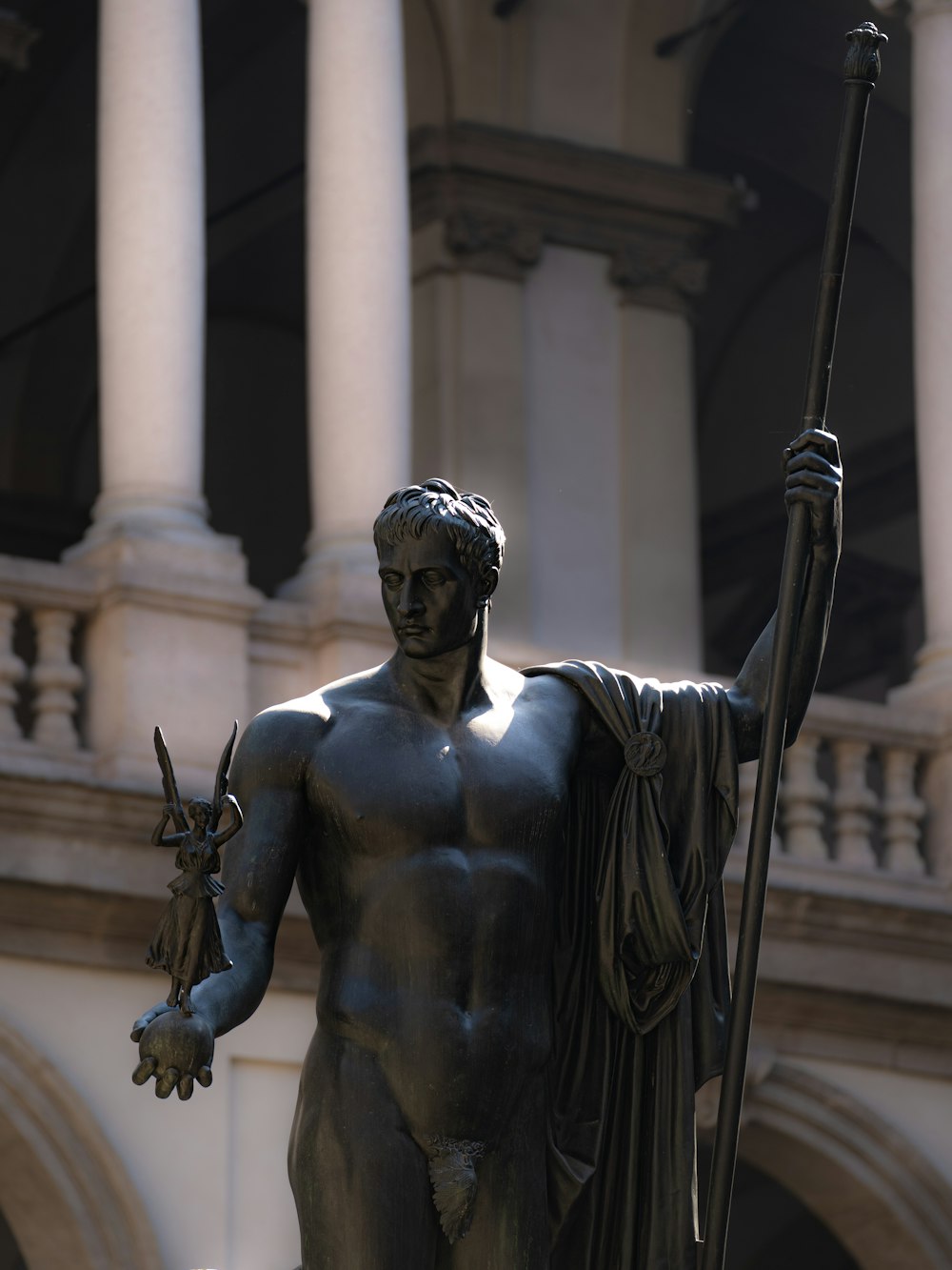 Una estatua de un hombre sosteniendo un bastón frente a un edificio