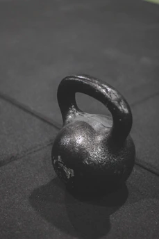 A sleek black kettlebell resting on a dark textured gym floor under moody lighting.