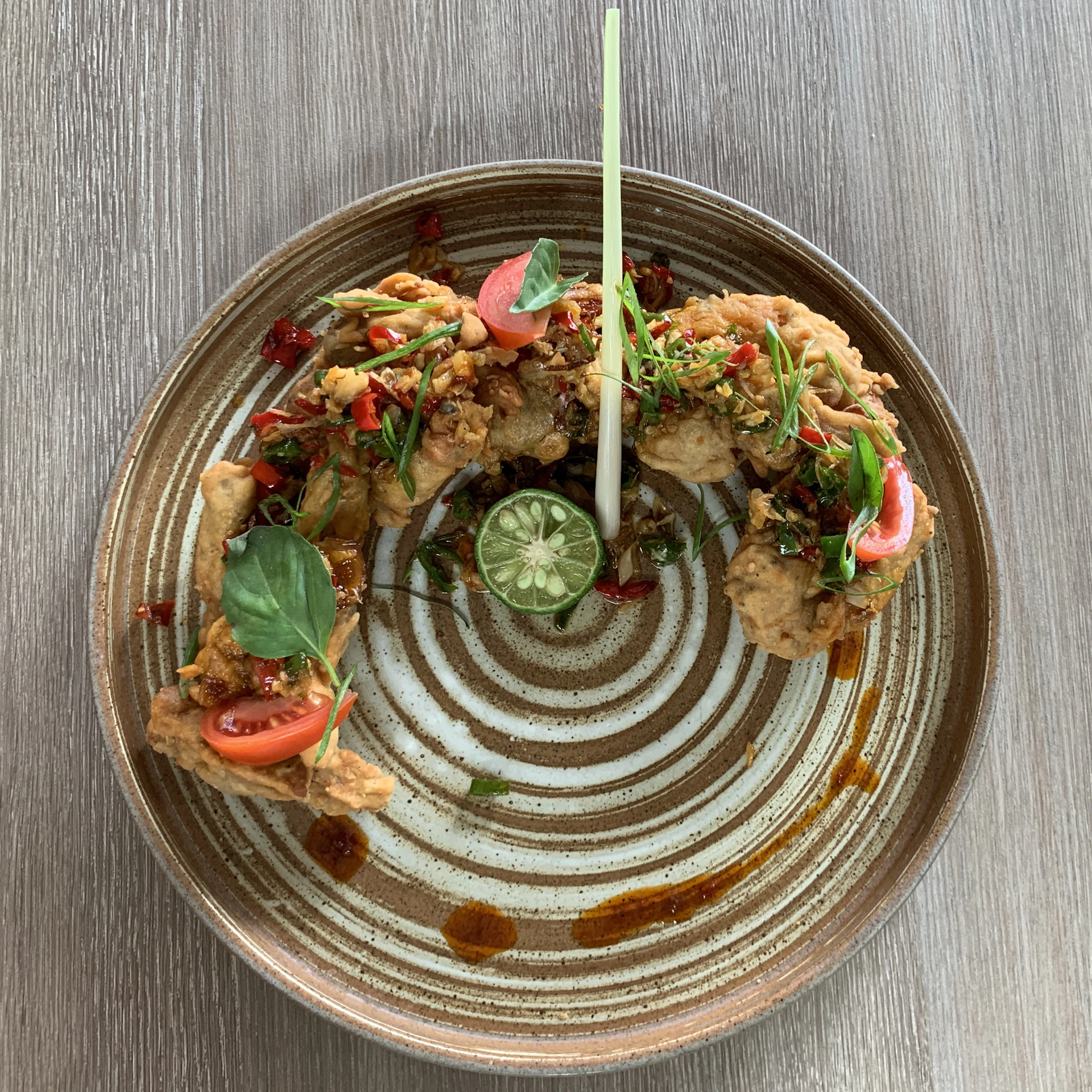 Close-up of crispy golden ayam pop served with sambal and fresh lime on a rustic wooden plate