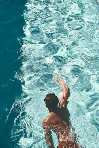 A vibrant photo of swimmers diving into a sparkling pool under a clear blue sky.